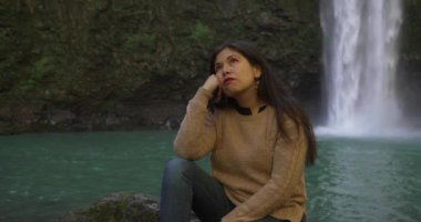 Meksikalı kadın, arkasında şelale olan bir kayanın üzerinde otururken meditasyon yapıyor.