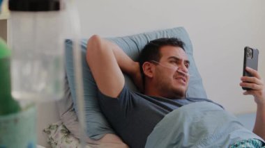Solunum cihazı ve oksijen tüpü olan mutlu bir Meksikalı adam telefonundan video görüşmesi yapıyor.