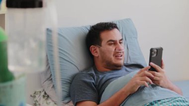 Solunum cihazı ve oksijen tüpü olan ciddi bir Meksikalı adam telefonundan video görüşmesi yapıyor.
