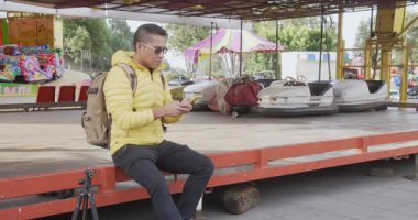 Meksikalı bir adam çarpışan arabaların yanında otururken akıllı telefonuyla yazıyor.