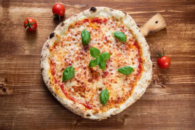 Domatesli pizza, ahşap arka planda peynir ve fesleğen.