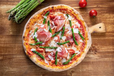 pizza with ham, arugula and tomatoes on wooden background