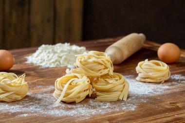 raw pasta with flour and ingredients on wooden background