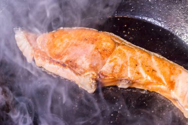 salmon cooked in a frying pan and smoking.