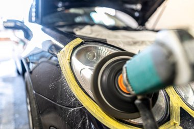 A mechanic polishes the headlights of a car.