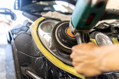 A mechanic polishes the headlights of a car.
