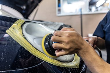 A mechanic polishes the headlights of a car.