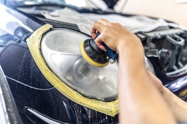 A mechanic polishes the headlights of a car.