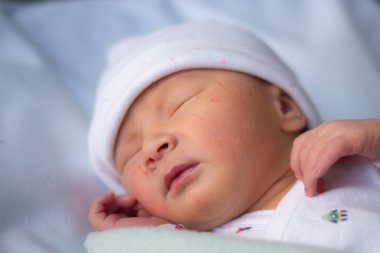 Doğumdan saatler sonra hastanenin beşiğinde sessizce yatan, Asya kökenli beyaz ırktan sevimli küçük bir kızın portresi.