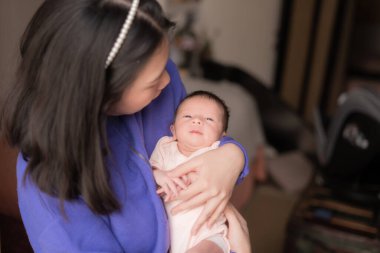 Genç ve mutlu Asyalı Çinli kadın, yeni doğmuş bebeğini şefkatle kucağına aldı. Annesi ve kızı sevgi ve ilgi kavramlarıyla.