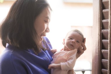 Genç ve mutlu Asyalı Çinli kadın, yeni doğmuş bebeğini şefkatle kucağına aldı. Annesi ve kızı sevgi ve ilgi kavramlarıyla.