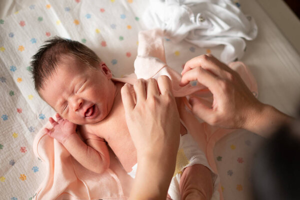mother hands changing diaper and clothes to beautiful and adorable newborn baby girl with mixed Asian Caucasian ethnicity in sweet face expression days after coming to life