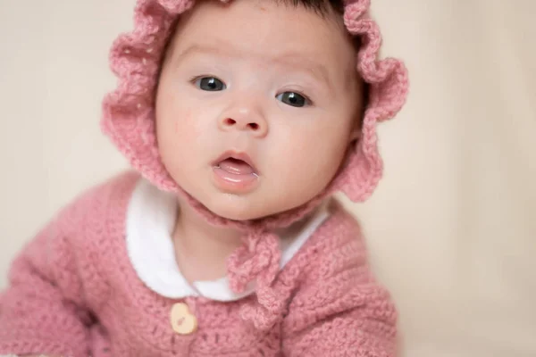 beautiful portrait of adorable mixed ethnicity Asian Caucasian baby girl a few weeks old lying on white blanket wearing a sweet pink hat in new life and newborn concept