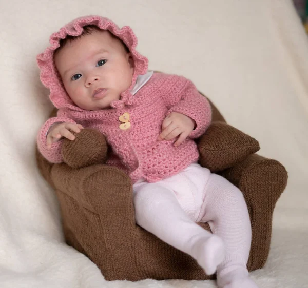 sweet portrait of adorable mixed ethnicity Asian Caucasian baby girl a few weeks old sitting on mini sofa couch wearing a sweet pink hat and jacket