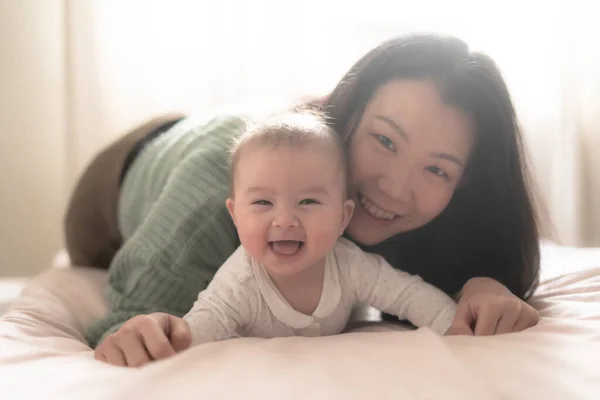愛と遊び心に満ちた若いアジア系韓国人女性は ベッドの上で赤ちゃんの女の子と楽しく交流しています 彼らの笑いは 純粋な幸福の中で大切な思い出をつなぐ — ストック写真