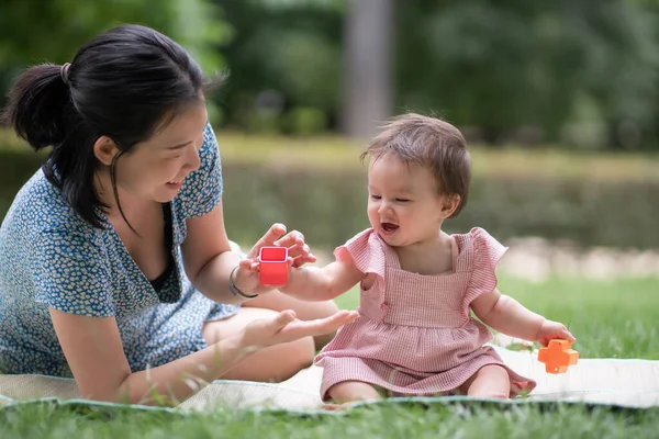 stock image outdoors lifestyle portrait of mother and daughter - young happy and sweet Asian Korean woman playing with her 8 months baby girl on grass at city park