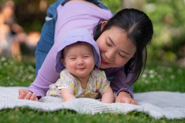 Şehir parkında 5 aylık mutlu ve sevimli bir kız bebek ve onun Asyalı Çinli kadını aşkta yemyeşil çimenler ve anne kız arasında neşeli bir anı paylaşıyorlar.
