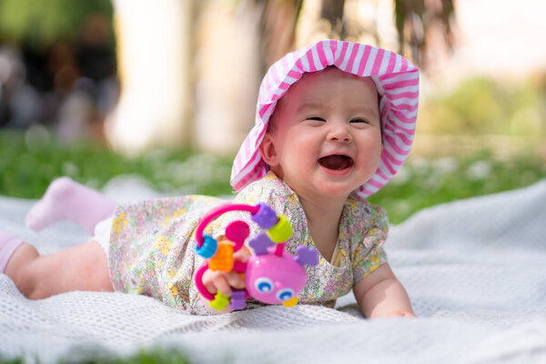 adorable and happy baby girl in summer hat embraces the joys of playfulness on a soft blanket playing with little toy. Laughing as she explores the natural wonders of an outdoors city park
