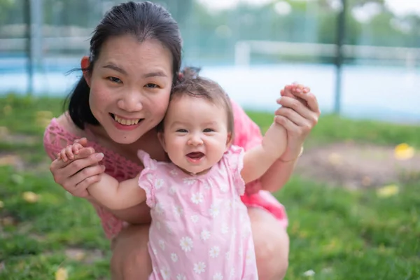Asian mum and little child - young happy and beautiful Chinese woman playing on city park with adorable and cheerful baby girl in mother and daughter love and bonding