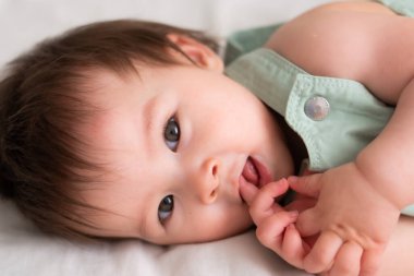 Karışık etnik köken Asyalı Kafkasyalı 8 aylık bebek - tapılası ve mutlu bir kadın çocuğun yaşam tarzı portresi yatakta şakacı bir şekilde yatarak çevreyi keşfediyor.