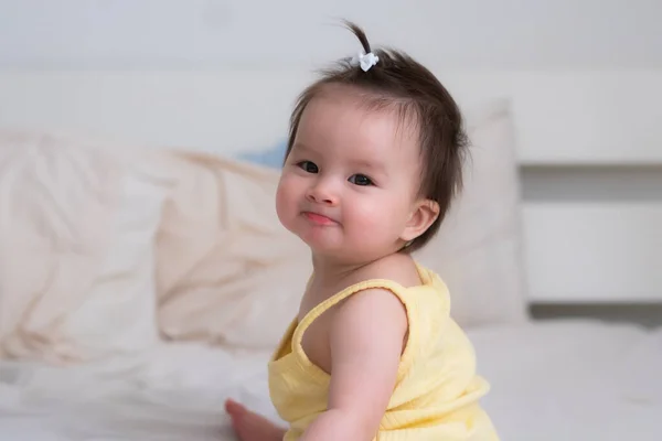 mixed ethnicity Asian Caucasian baby girl sitting on bed - sweet and adorable little baby 8 months old with a funny pony tail looking around curious