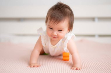 9 aylık karışık etnik kökenli Asyalı bebek portresi. Mutlu ve tasasız oynuyor. Yatakta emekliyor ve çocukluk ve çocuk odası konseptinde renk engelleriyle uğraşıyor.