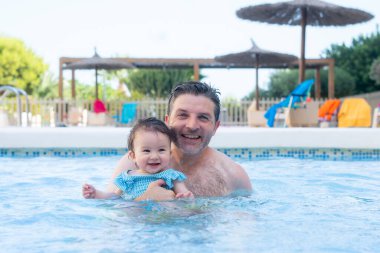 Baba ve küçük kızın hayat tarzı portresi. Yaz tatilinin tadını çıkaran bir adam, tatlı bebeğini kucağında tutuyor. Heyecanlı ve neşeli bir şekilde havuzda birlikte oynuyor. 