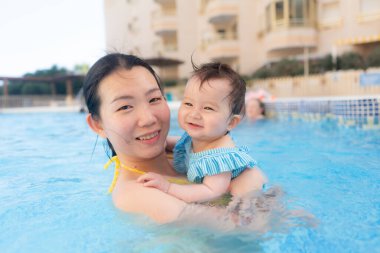 Mutlu ve güzel Asyalı kadın kucağında küçük bebeğiyle Koreli anne ve tatlı kızı yazın havuzda su üstünde oynuyorlar.