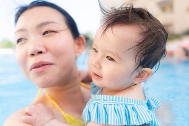 Mutlu ve güzel Asyalı kadın kucağında küçük bebeğiyle Koreli anne ve tatlı kızı yazın havuzda su üstünde oynuyorlar.