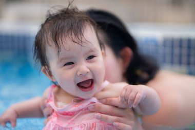 Mutlu ve güzel Asyalı kadın kucağında küçük bebeğiyle Koreli anne ve tatlı kızı yazın havuzda su üstünde oynuyorlar.