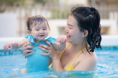 Mutlu ve güzel Asyalı kadın kucağında küçük bebeğiyle Koreli anne ve tatlı kızı yazın havuzda su üstünde oynuyorlar.
