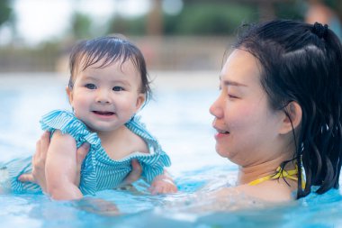 Mutlu ve güzel Asyalı kadın kucağında küçük bebeğiyle Koreli anne ve tatlı kızı yazın havuzda su üstünde oynuyorlar.