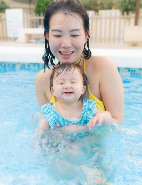 Mutlu ve güzel Asyalı kadın kucağında küçük bebeğiyle Koreli anne ve tatlı kızı yazın havuzda su üstünde oynuyorlar.