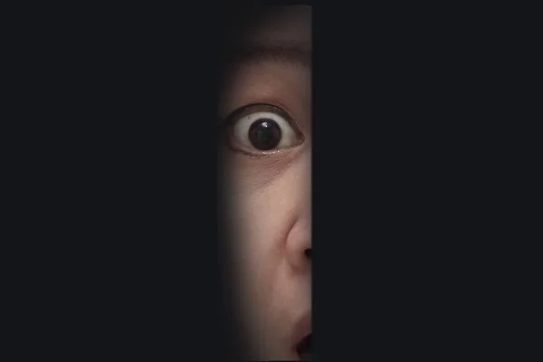 Shocked person with big eyes and mouth open, peeking trough open door in the dark room