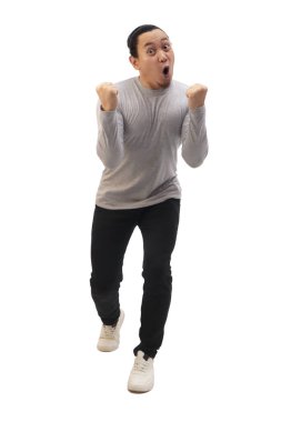 Gri gömlekli, siyah kot ve beyaz ayakkabılı bir adam zaferi kutluyor, elini kaldırıyor ve kazanıyor. Tüm vücut portresi izole edildi.