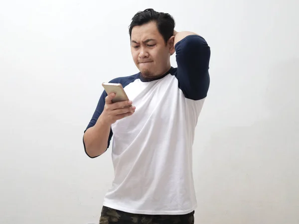 Asian man looking at his phone with upset displeased expression, male person just receiving bad news, against grey background