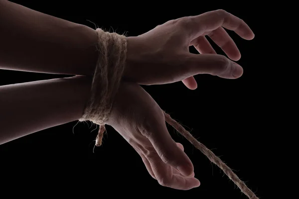 Person hands tied with rope isolated on black dark background, captive victim restrained concept