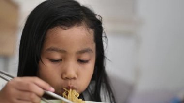 Asian little girl eating noodle with chopstick, children enjoys her meal, face close up shot