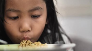 Asian little girl eating noodle with chopstick, children enjoys her meal, face close up shot
