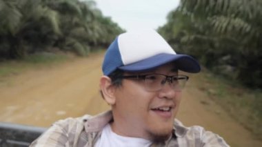 Asian man talking to camera while ride on a open truck in the rural area dirt road, traveler backpacker making vlog in remote area, slow motion