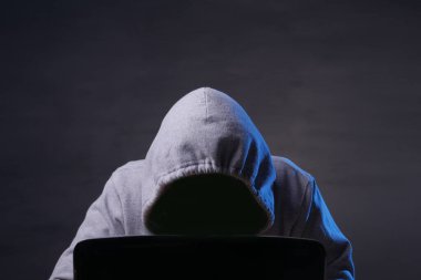 Hacker karanlıkta dizüstü bilgisayar kullanarak gri kapüşonlu giyer.