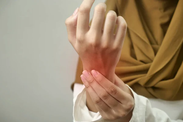 Anonymous woman touching her wrist, suferring from arthritis disease, close up against grey background