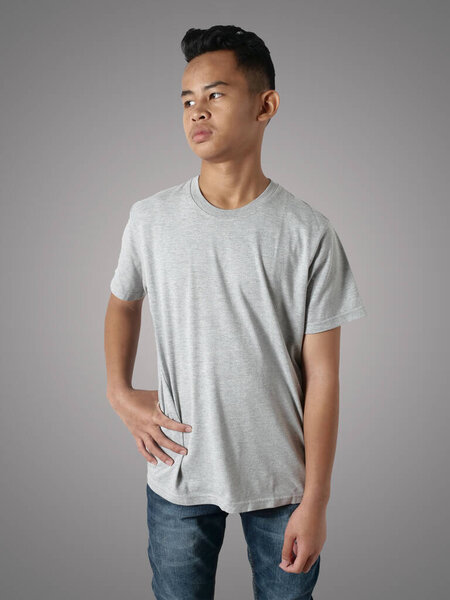 Young Asian teenage boy wearing grey shirt, standing with hands on hip over gray background, t-shirt template mock up