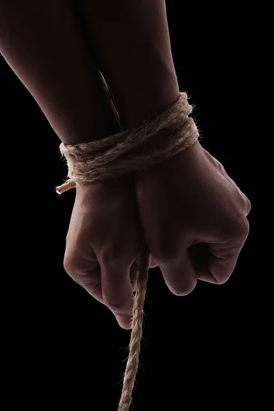 Person hands tied with rope isolated on black dark background, captive victim restrained concept
