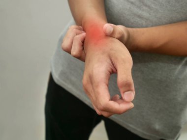 Kimliği belirsiz biri bileğine dokunuyor, eklem iltihabından muzdarip, gri arkaplana yakın duruyor.