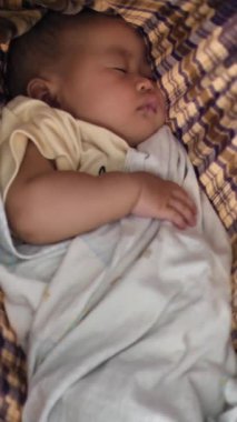 Küçük Asyalı kız bebek geleneksel sallanan kumaş beşiğinde uyuyor.