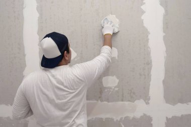 Sıva işi ve duvar boyası hazırlığı. Asyalı erkek alçı yapıyor veya alçıpan yamasını dolduruyor