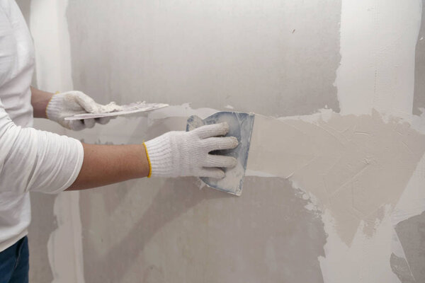 Plasterwork and wall painting preparation. Asian male applying plaster or filling drywall patch