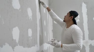 Sıva işi ve duvar boyası hazırlığı. Asyalı erkek alçı yapıyor veya alçıpan yamasını dolduruyor
