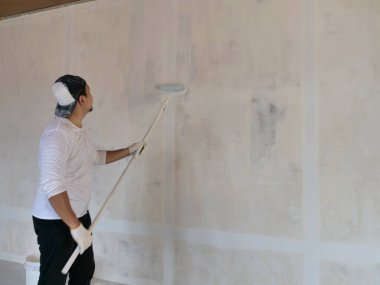 Asyalı erkek ressam paten fırçasıyla yeni bir beyaz duvar boyuyor, ev dekorasyonu konsepti.